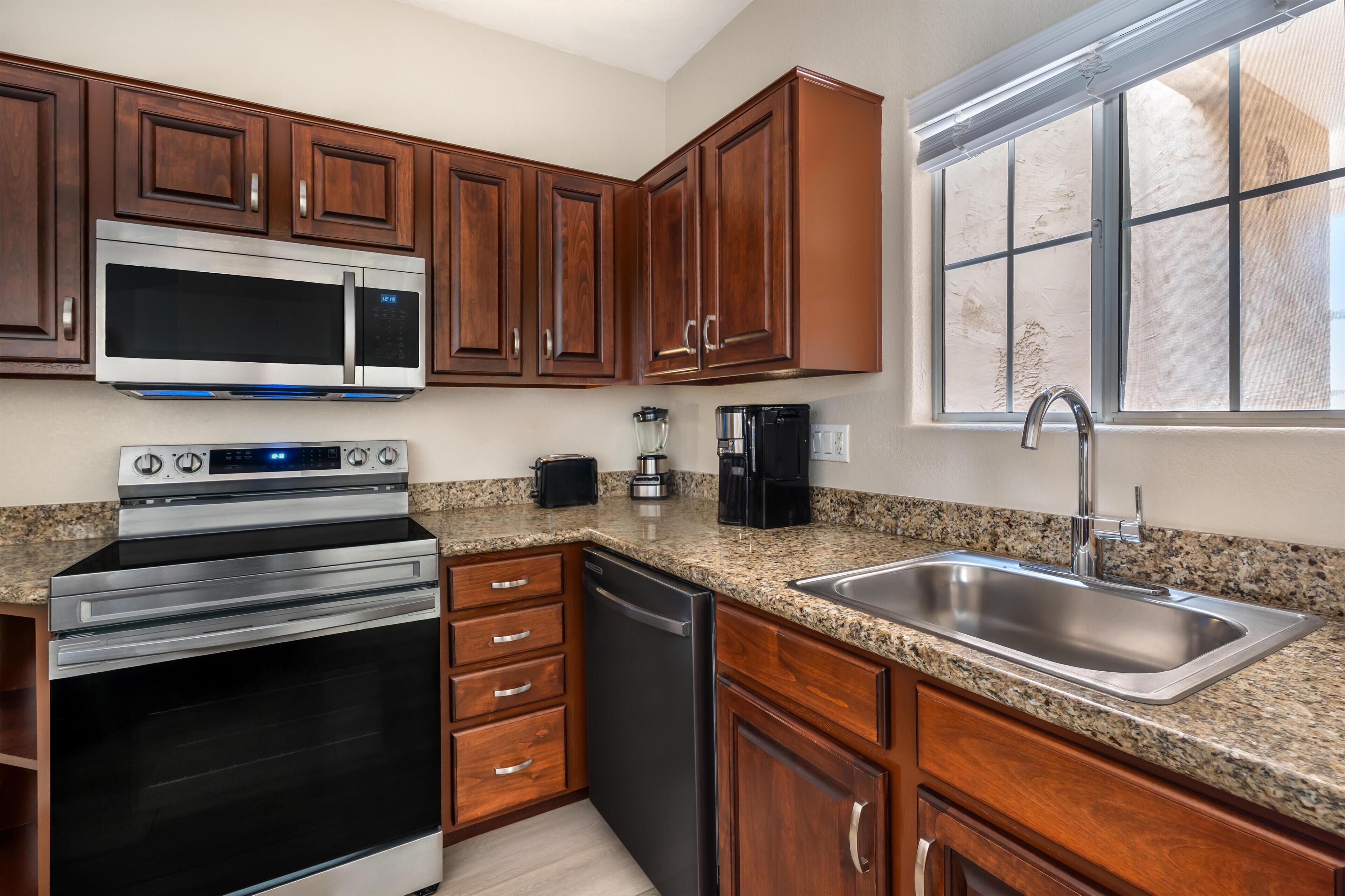 A kitchen with wooden cabinets, stainless steel appliances, granite countertops, and a window with blinds.