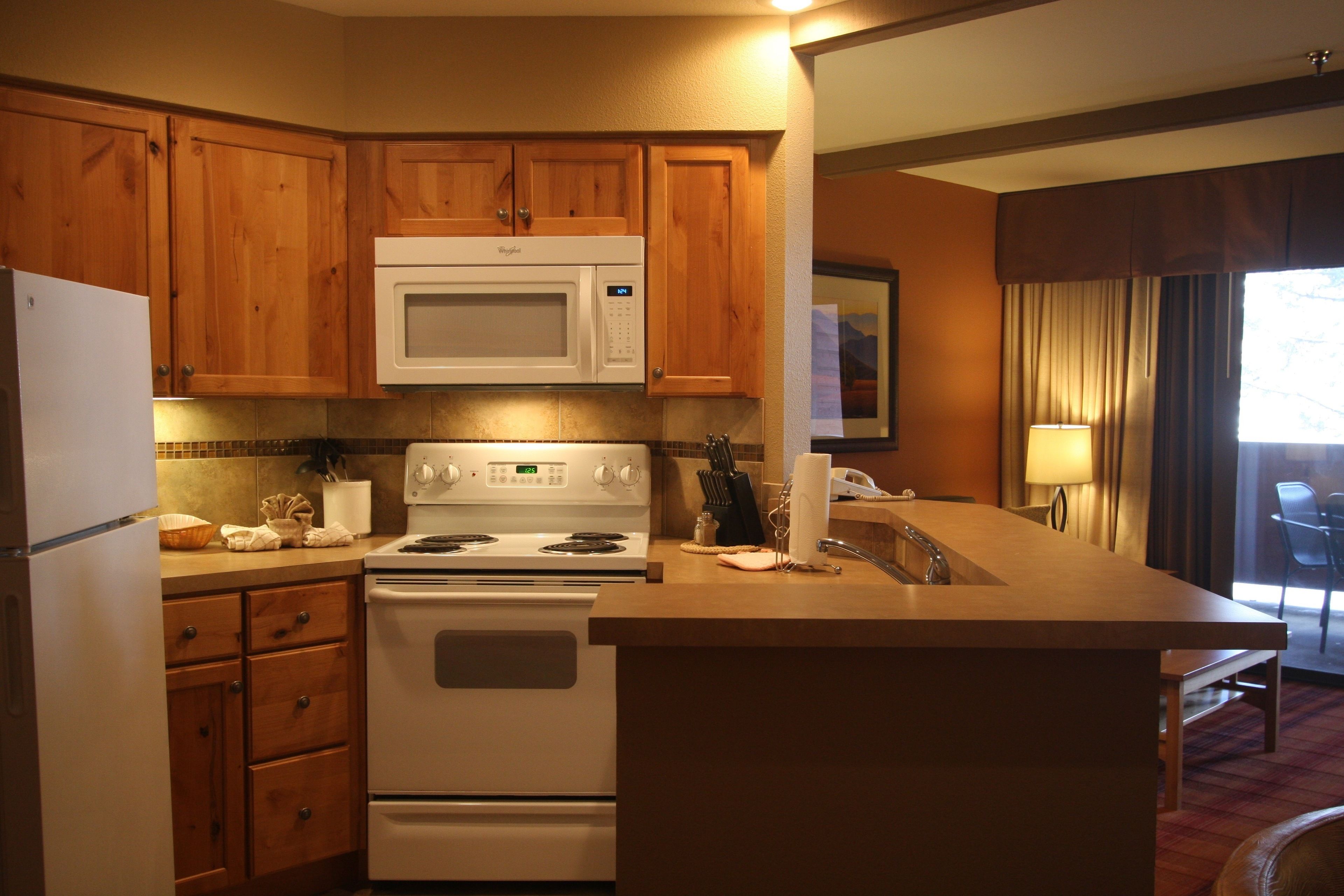 A kitchen with wooden cabinets, a microwave, stove, and a sink.