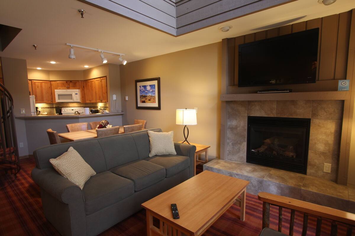 A living room with a sofa, a coffee table, a fireplace, and a TV mounted above it.