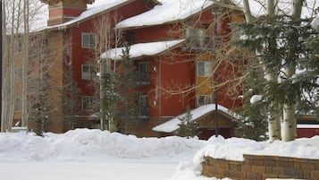 A multi-story building with a red facade, snow-covered roof, and a brick wall in the foreground.