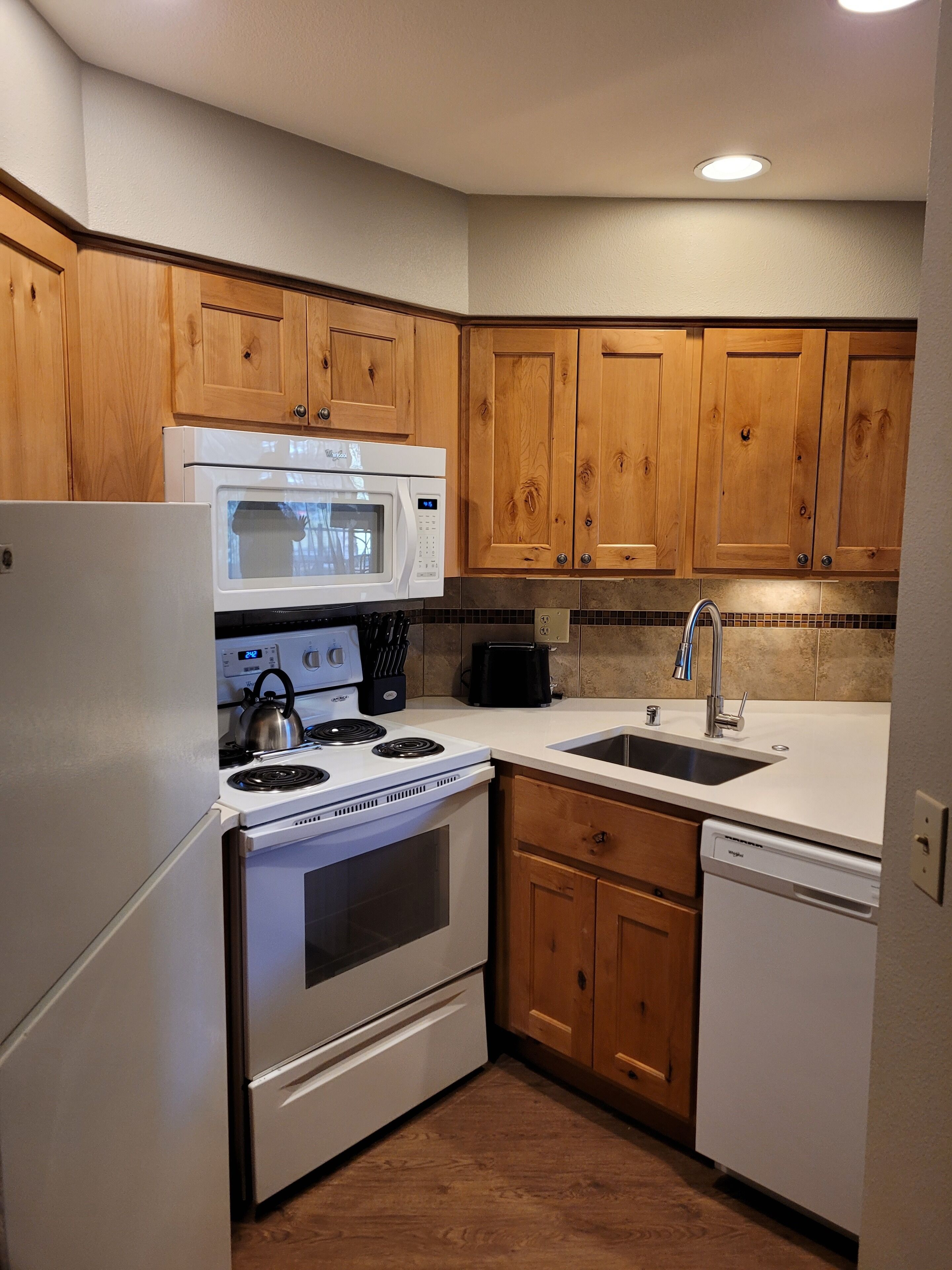 A compact kitchen with wooden cabinets, a white stove, a microwave, a sink, and a dishwasher.
