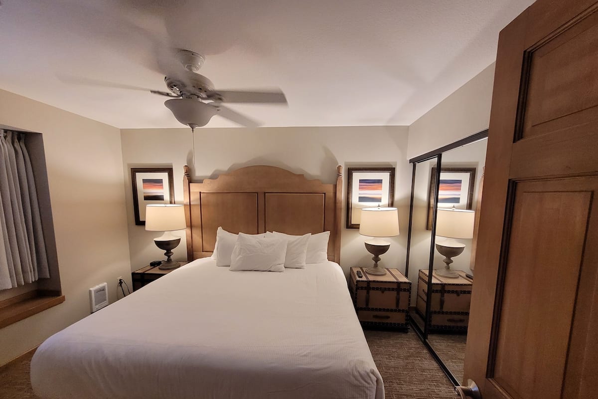 A hotel room with a large bed, a ceiling fan, two bedside tables with lamps, and a large mirror.