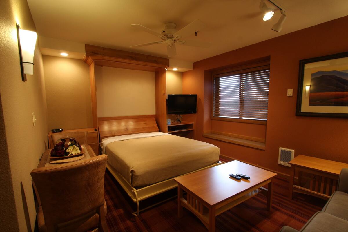A hotel room with a bed, a desk, a chair, a television, and a window with blinds.