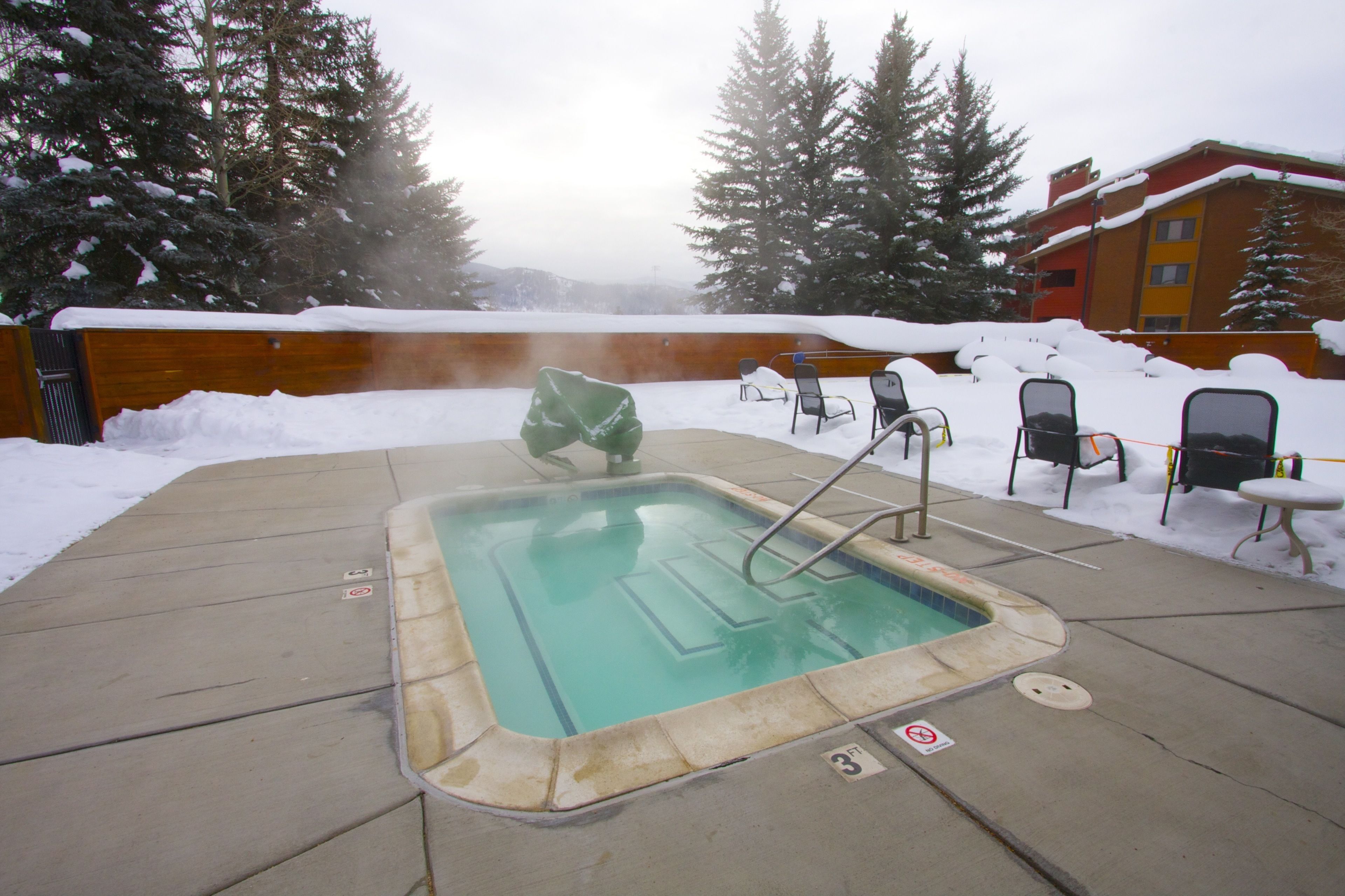 Un bain à remous doté d’une terrasse en bois, entouré d’un paysage enneigé et d’arbres.