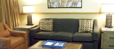 A living room with a sofa, armchair, ottoman, and two side tables with lamps.