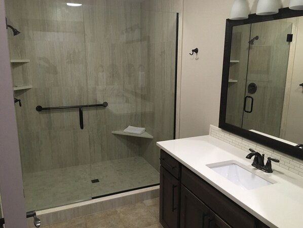 A modern bathroom with a glass shower enclosure, a white sink, dark cabinetry, and a large mirror.