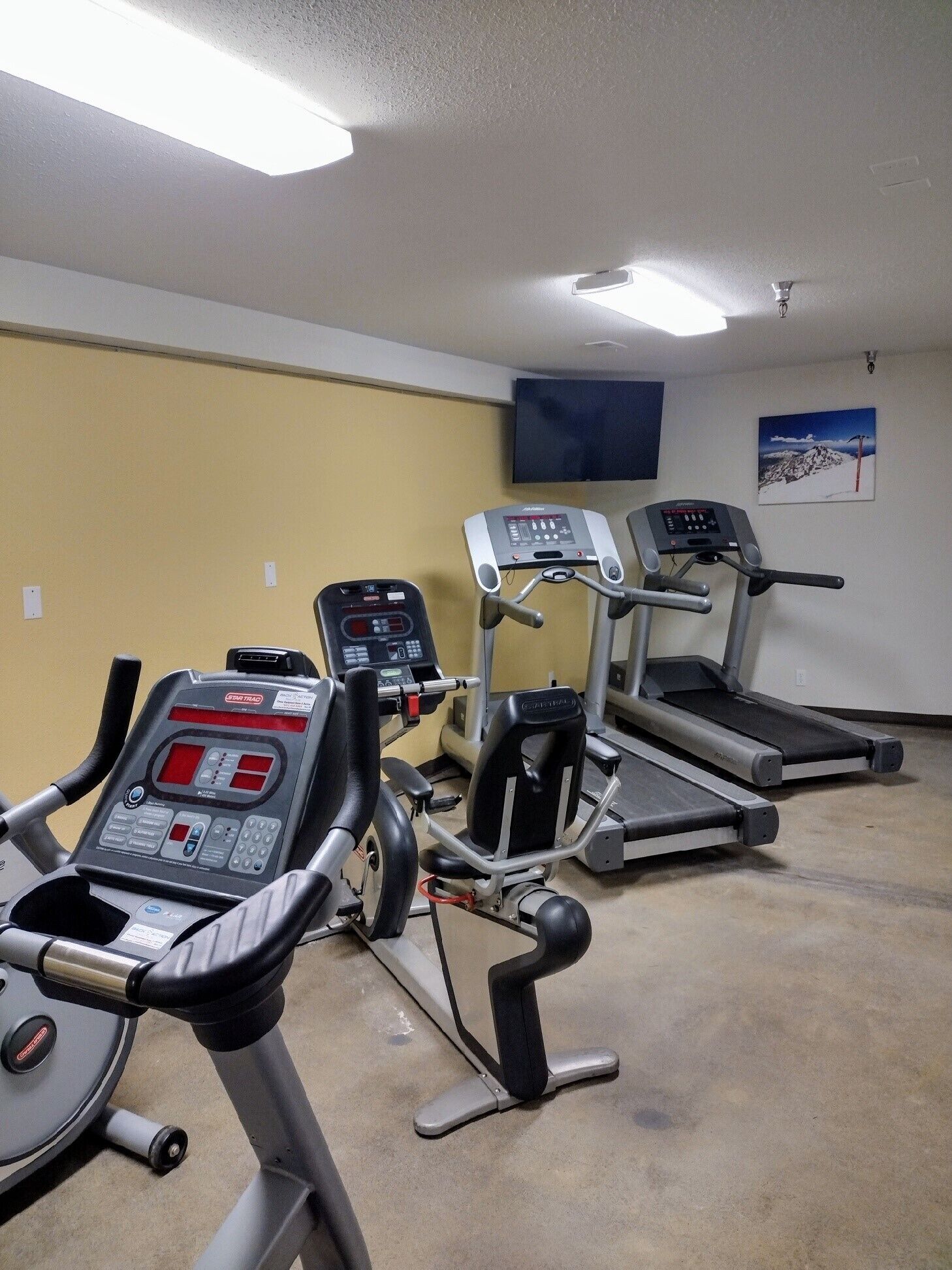 A gym with three treadmills, a stationary bike, and a weight machine.