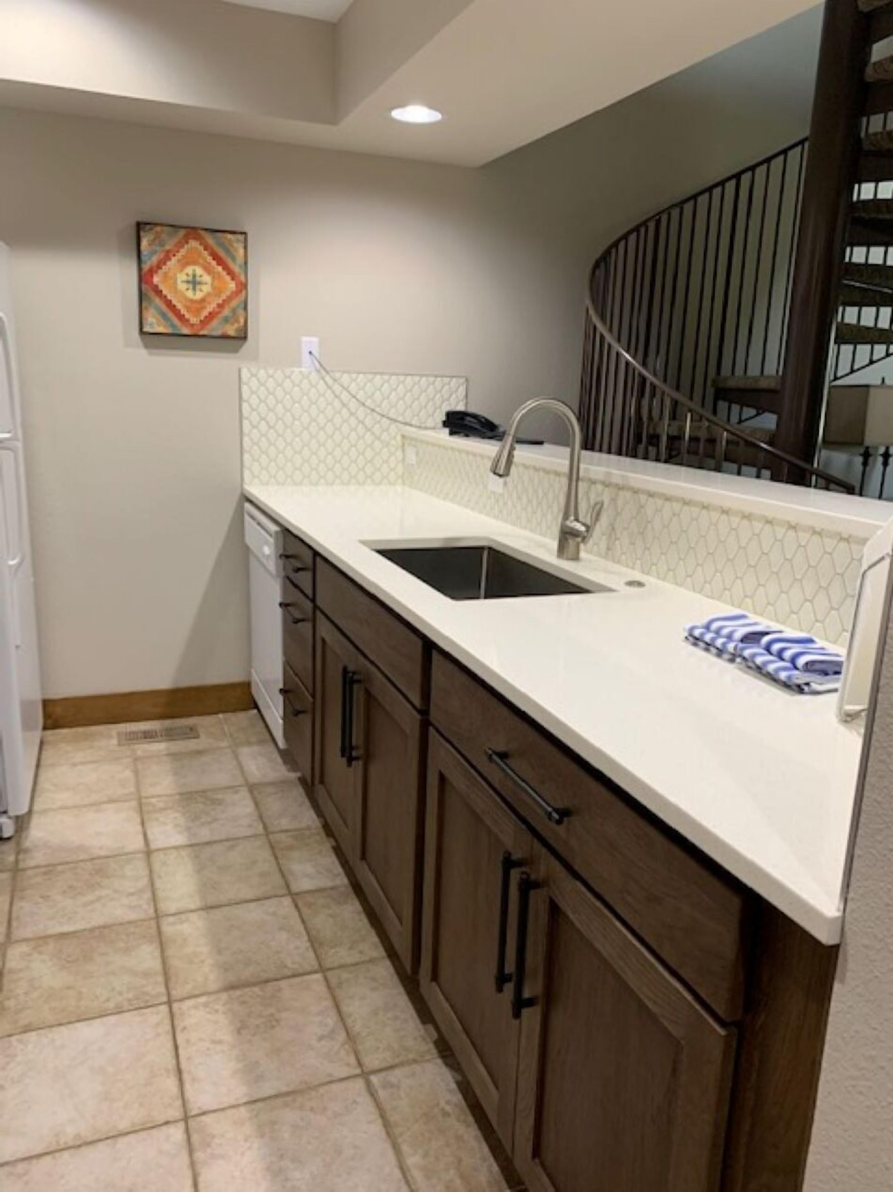 A kitchen with a white countertop, a sink, and wooden cabinets.