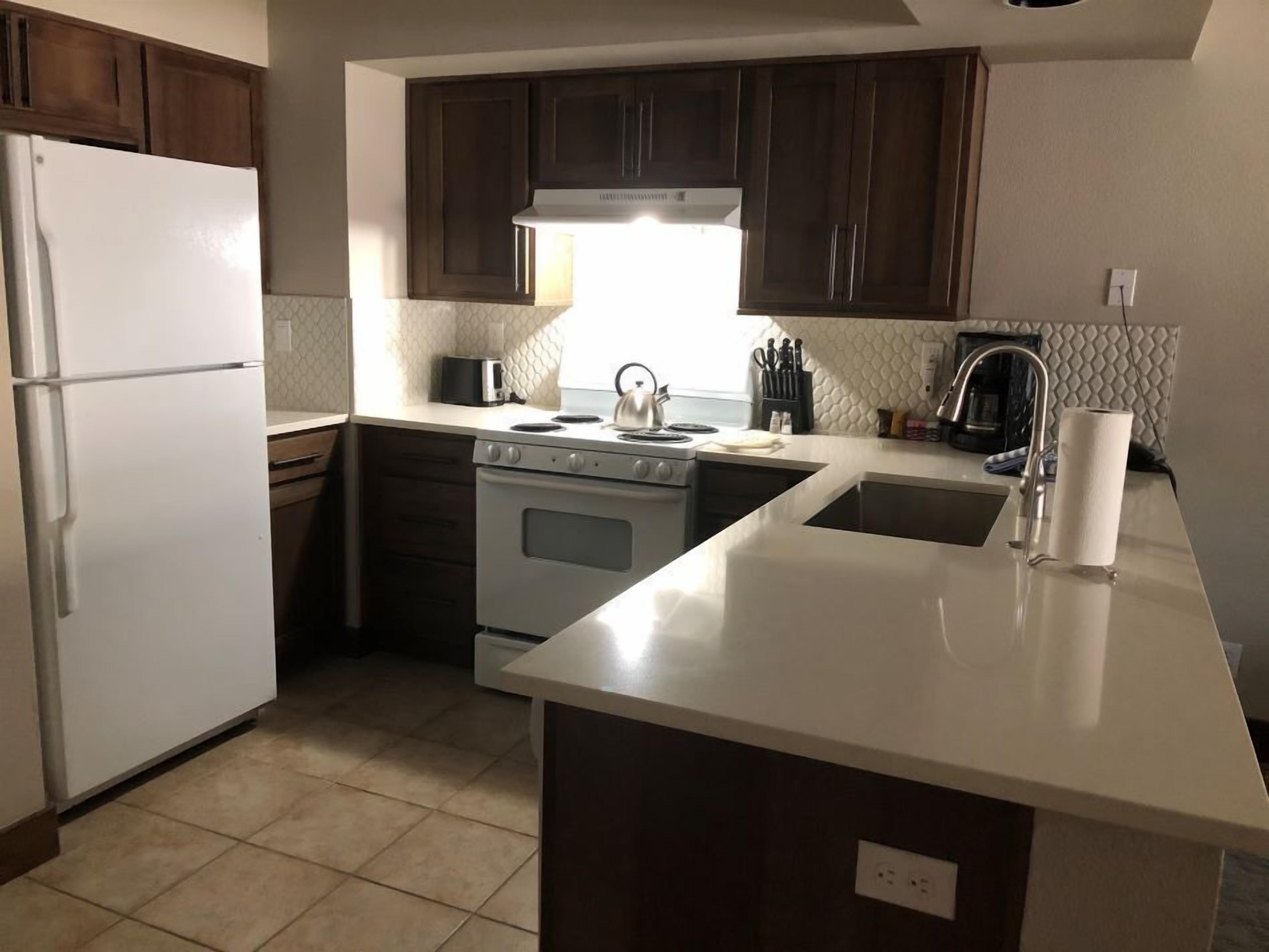 A kitchen with dark wooden cabinets, a white refrigerator, a stove, and a sink.