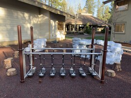 En metallkonstruktion med hjul, troligen en bagagevagn, i ett parkliknande område med träd och en byggnad i bakgrunden.