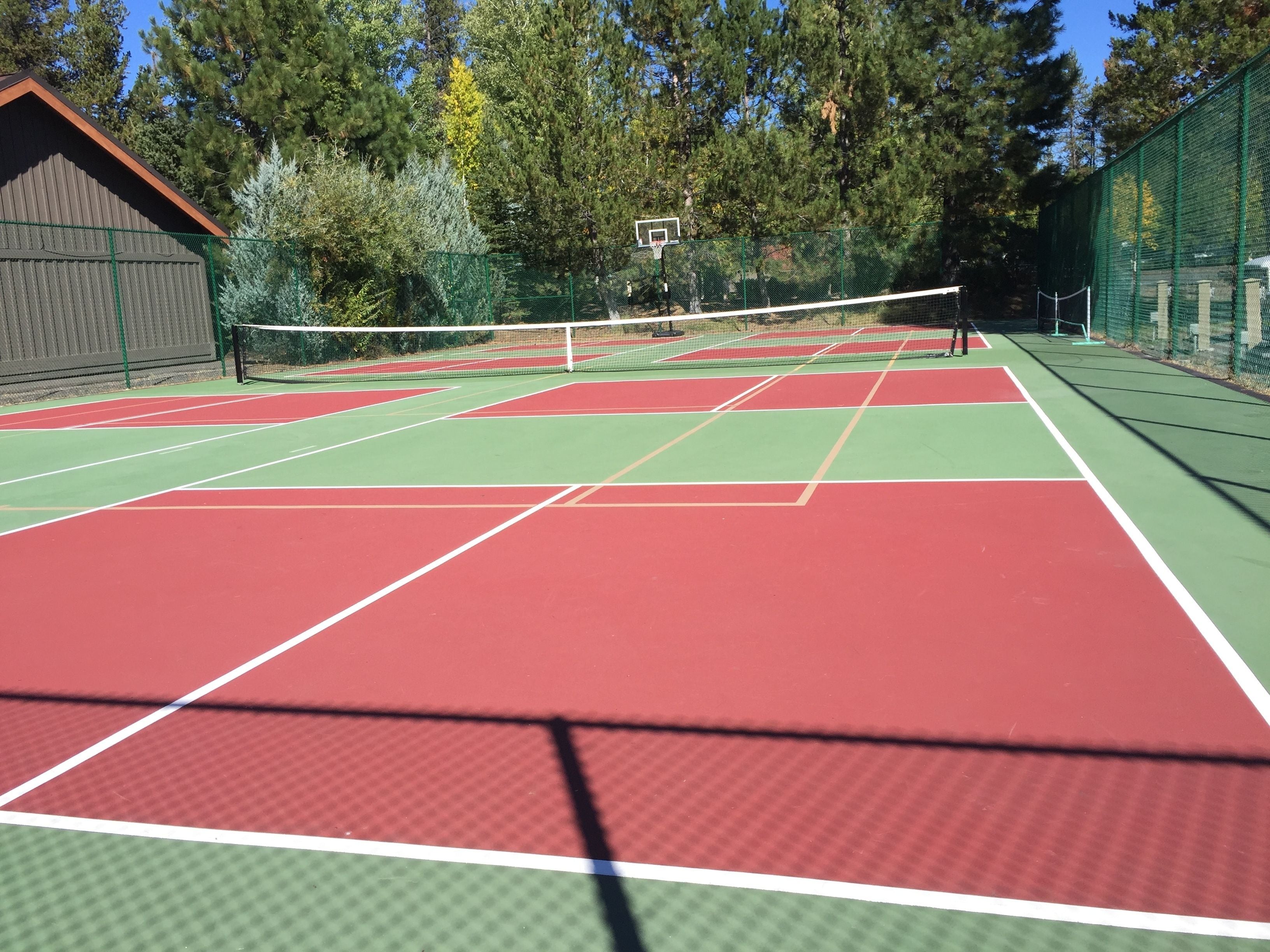 An outdoor tennis court with multiple courts, a net, and a basketball hoop.