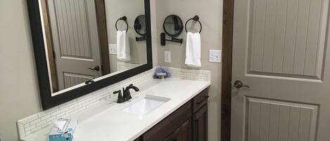A bathroom with a white sink, dark wooden cabinets, a large mirror, and a door with a light switch.