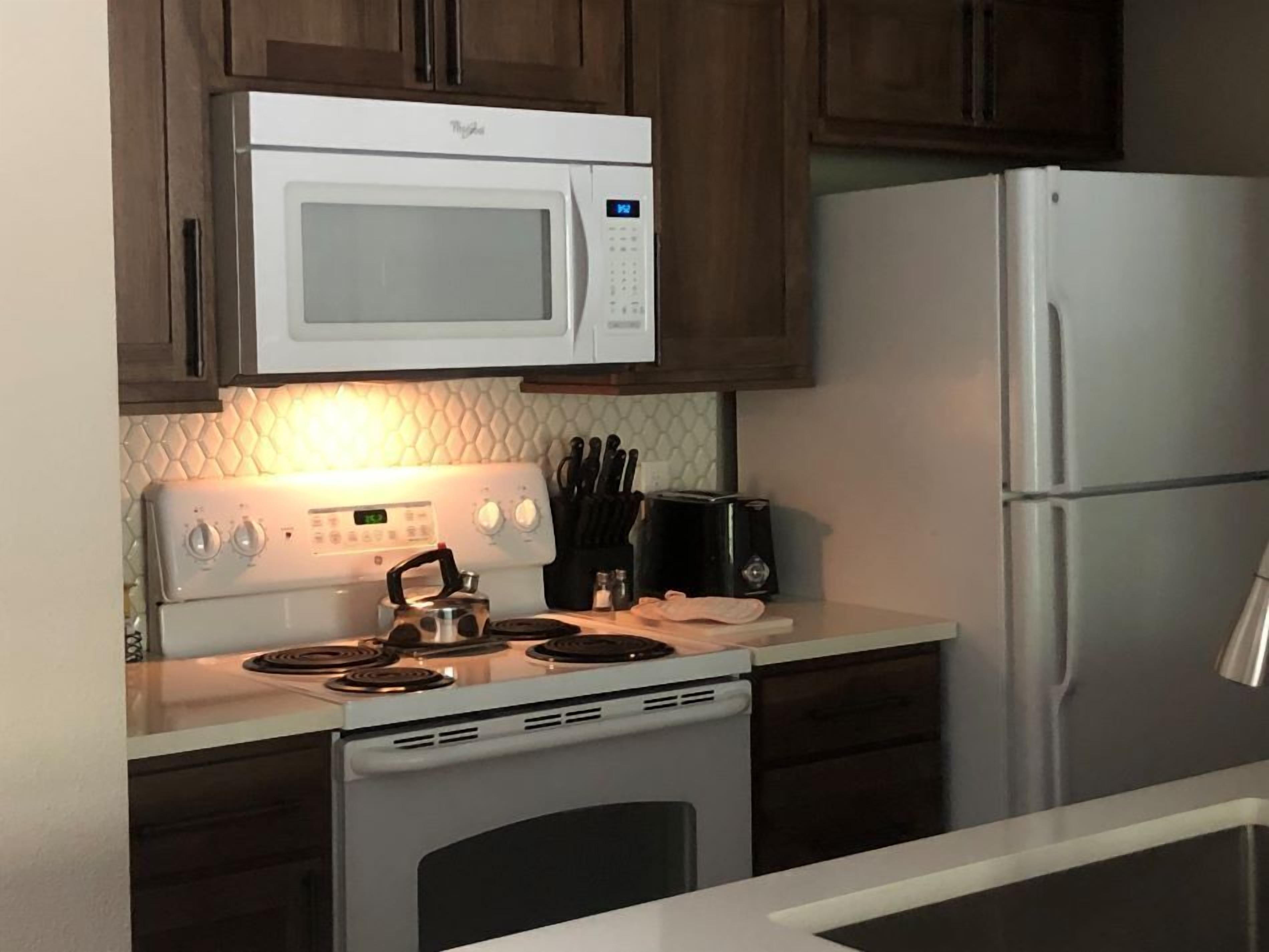 A kitchen with a white microwave, stove, and refrigerator. There is a toaster and a kettle on the counter.