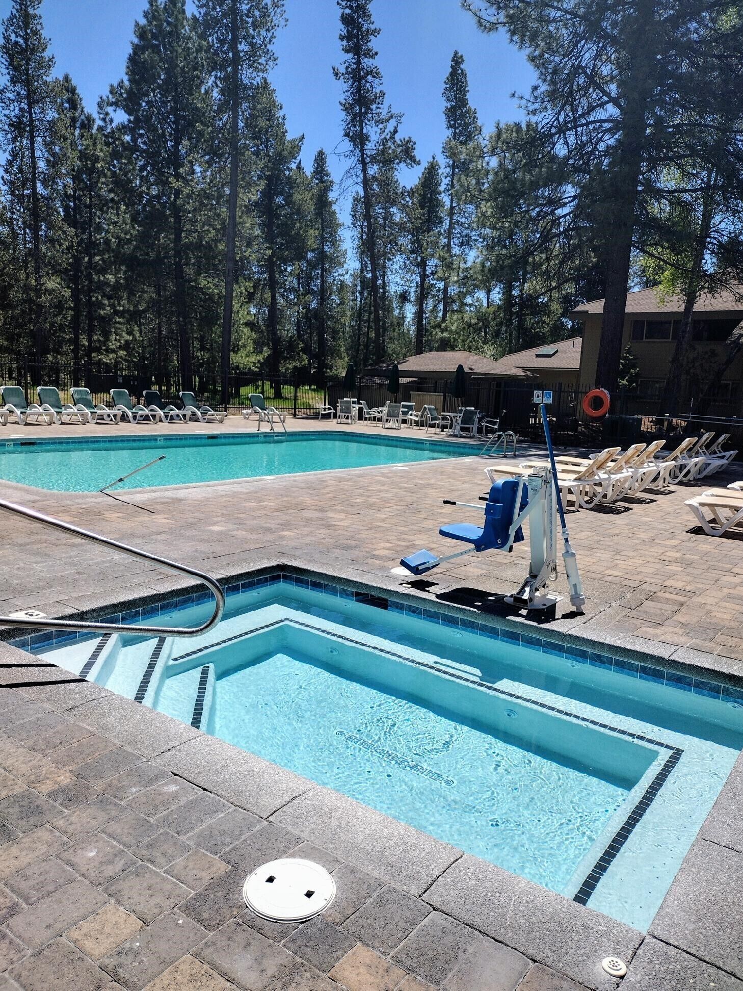 Une piscine dotée de chaises longues et d’une bouée de sauvetage, entourée d’arbres et d’un bâtiment.