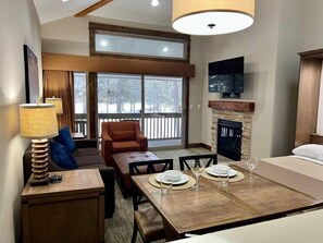 A modern living room with a fireplace, a dining table set for four, and a cozy seating area with a sofa and armchairs.