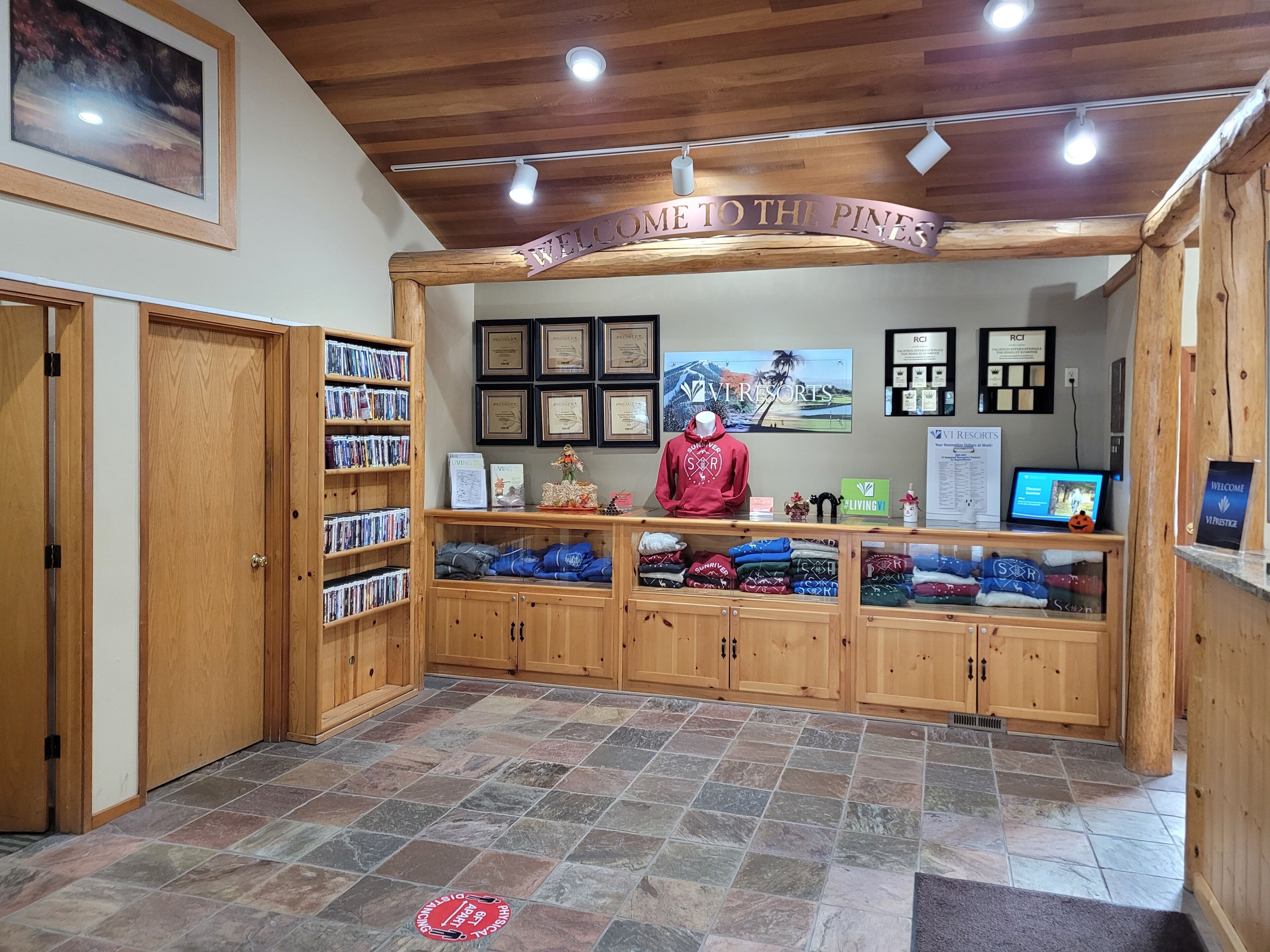 A reception area with a wooden counter, framed certificates, and a 'Welcome to the Pines' sign.