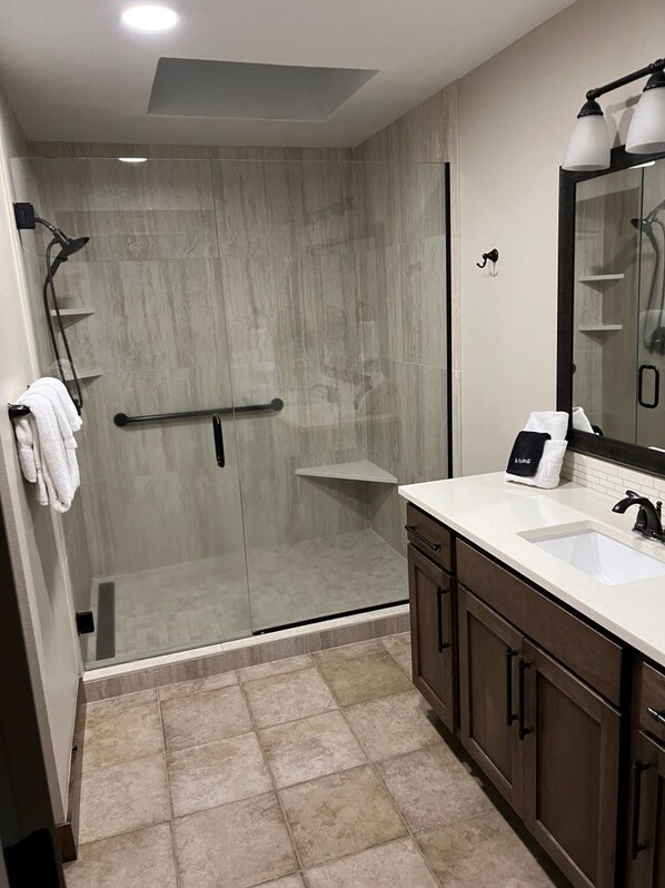 A modern bathroom with a glass shower enclosure, a vanity with a sink, and a large mirror.