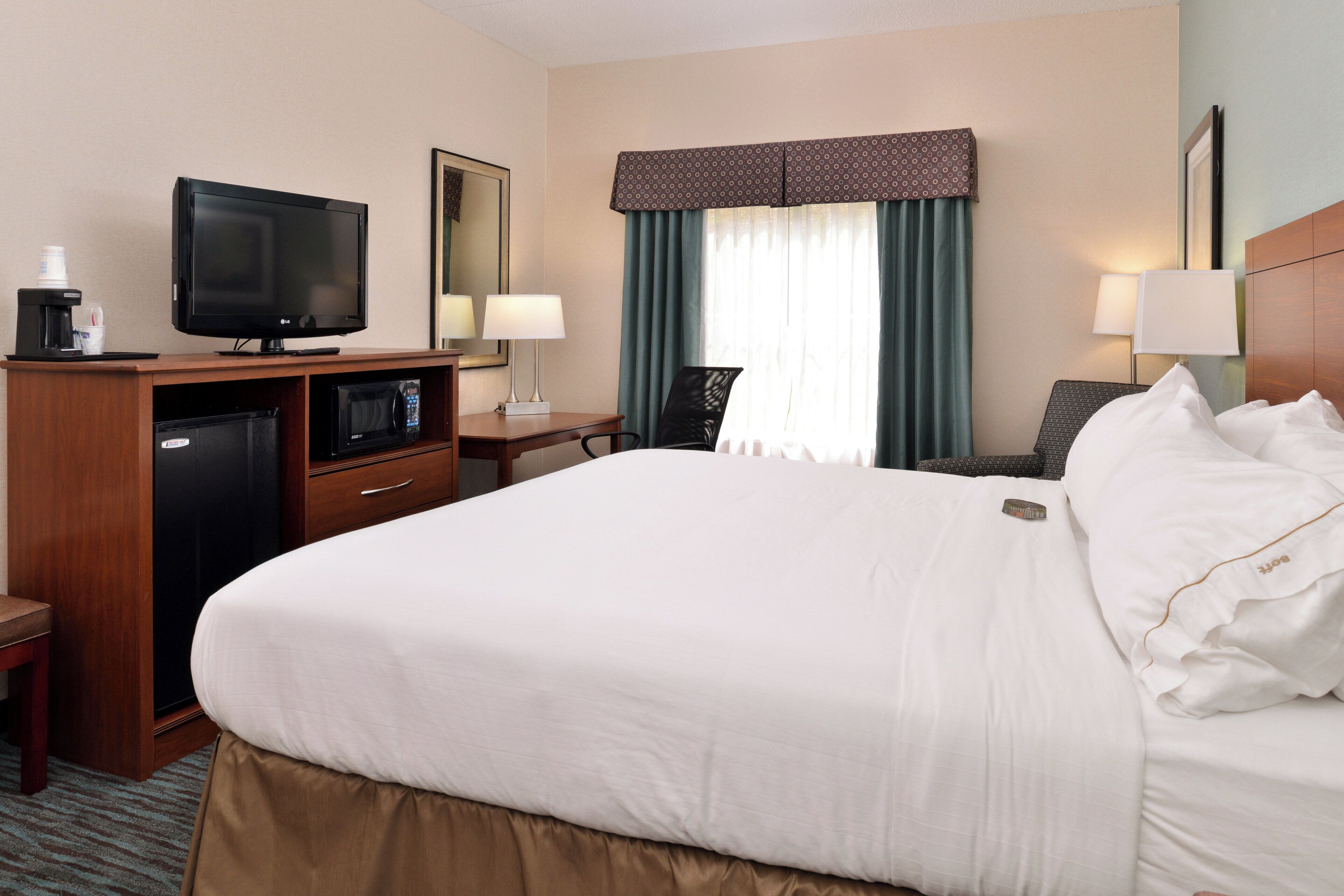 Hotelkamer met een bed, een bureau met een televisie, een koffiezetapparaat, een magnetron en een raam met gordijnen.