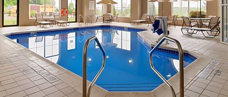 An indoor swimming pool with clear poolside areas, sun loungers, and umbrellas.