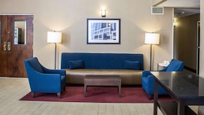 A hotel lobby with a blue sofa, two armchairs, a small table, and a red rug. There are four abstract paintings on the wall and a framed picture above the sofa. - Comfort Inn & Suites Fuquay Varina (Fuquay-Varina)