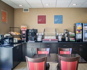 A breakfast area with a waffle maker, coffee machine, and juice dispenser. There are tables and chairs, and signs that read "YOUR morning sizzle" and "YOUR morning chill."