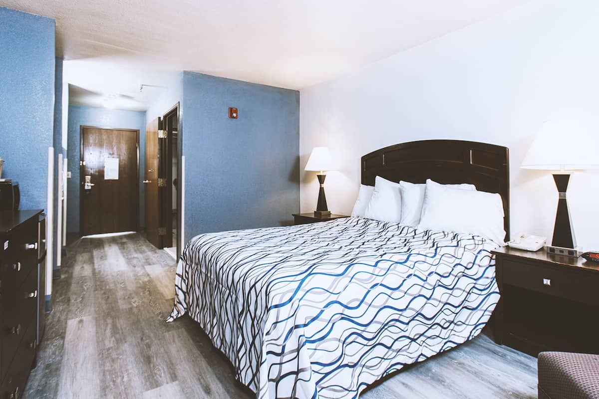 A hotel room with a large bed, two bedside tables with lamps, a dresser, and a door leading to another room.