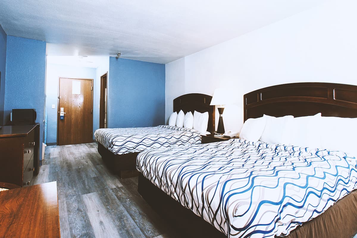 A hotel room with two beds, a wooden dresser, and a desk.