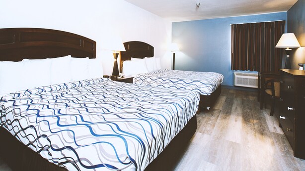 A hotel room with two beds, a desk, a chair, and a window with curtains.