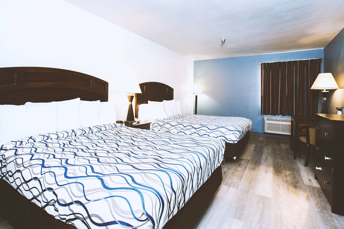 A hotel room with two beds, a desk, a chair, and a window with curtains.
