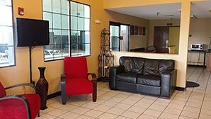A living room with a red chair, a black sofa, a TV, and a kitchen area in the background.