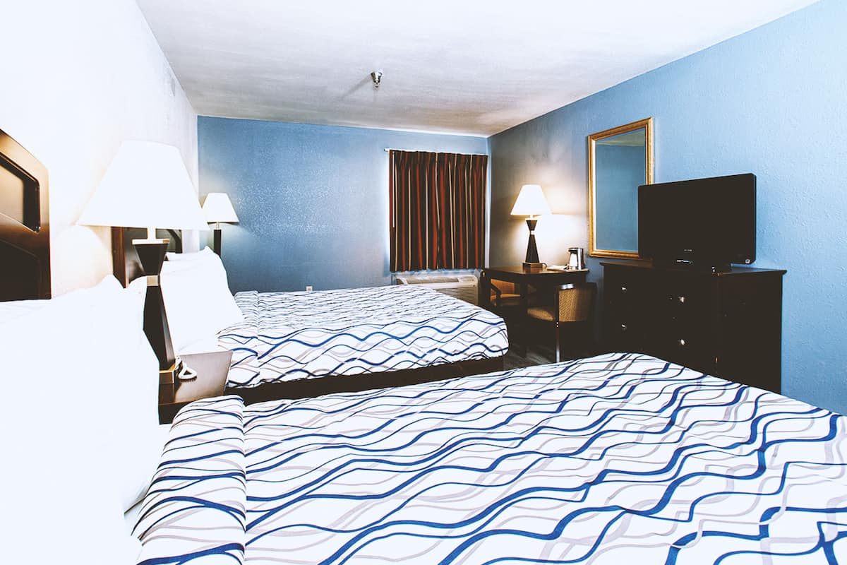 A hotel room with two beds, a television, a desk, and a mirror.