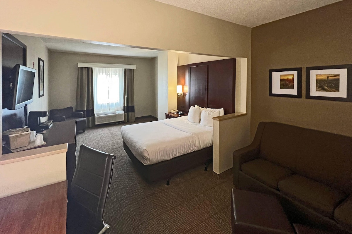 A hotel room with a bed, a desk with a chair, a television, and two framed pictures on the wall.