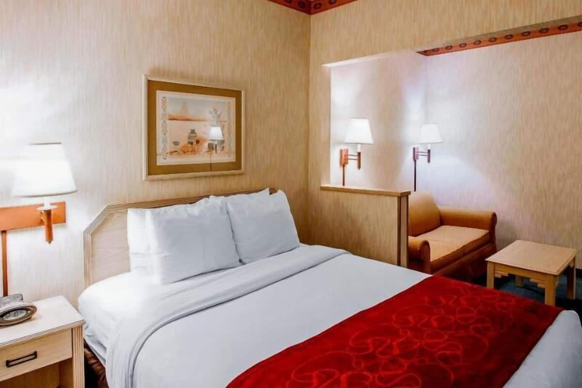A hotel room with a bed, a nightstand, a chair, a small table, and two wall-mounted lamps.