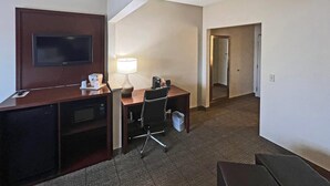 A hotel room with a desk, chair, lamp, television, and a small kitchenette. - Comfort Suites Peoria Sports Complex (Peoria)