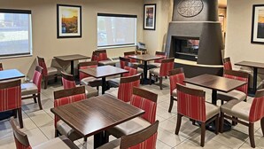 A restaurant with multiple tables and chairs, a fireplace, and framed pictures on the walls. - Comfort Suites Peoria Sports Complex (Peoria)