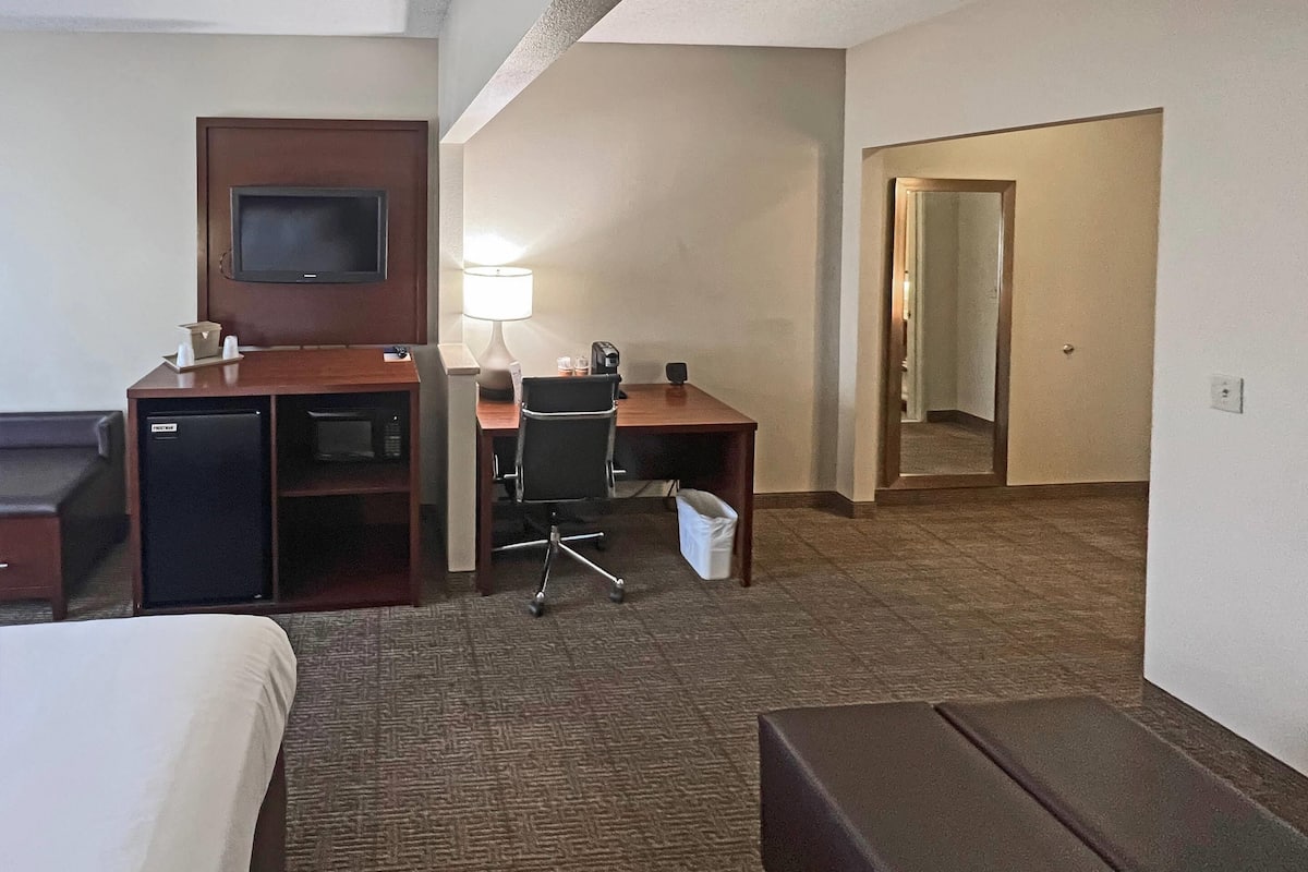 A hotel room with a bed, a desk with a computer, a TV, a lamp, and a trash bin.