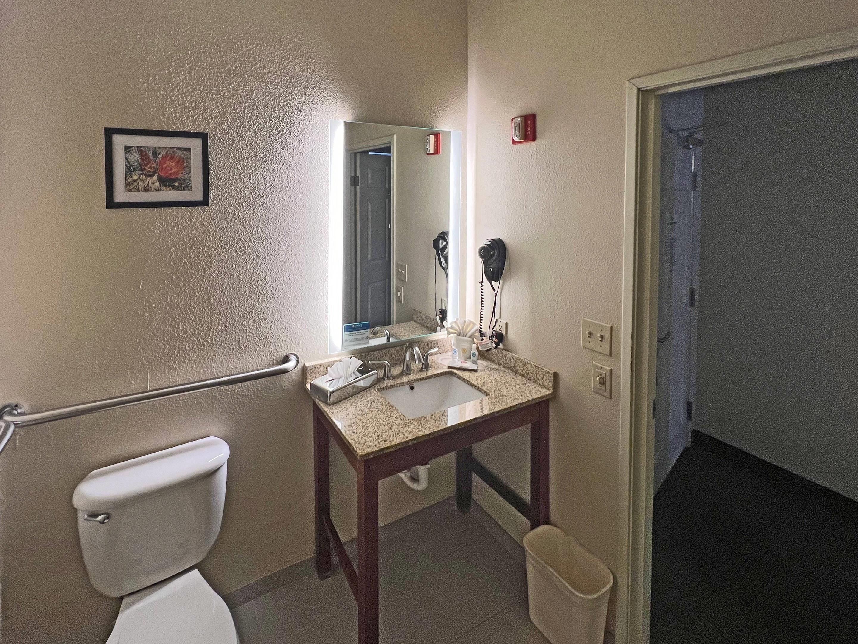 A bathroom with a toilet, sink, mirror, hairdryer, and a trash bin.