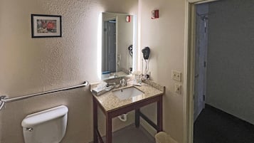 A bathroom with a toilet, sink, mirror, hairdryer, and a trash bin.