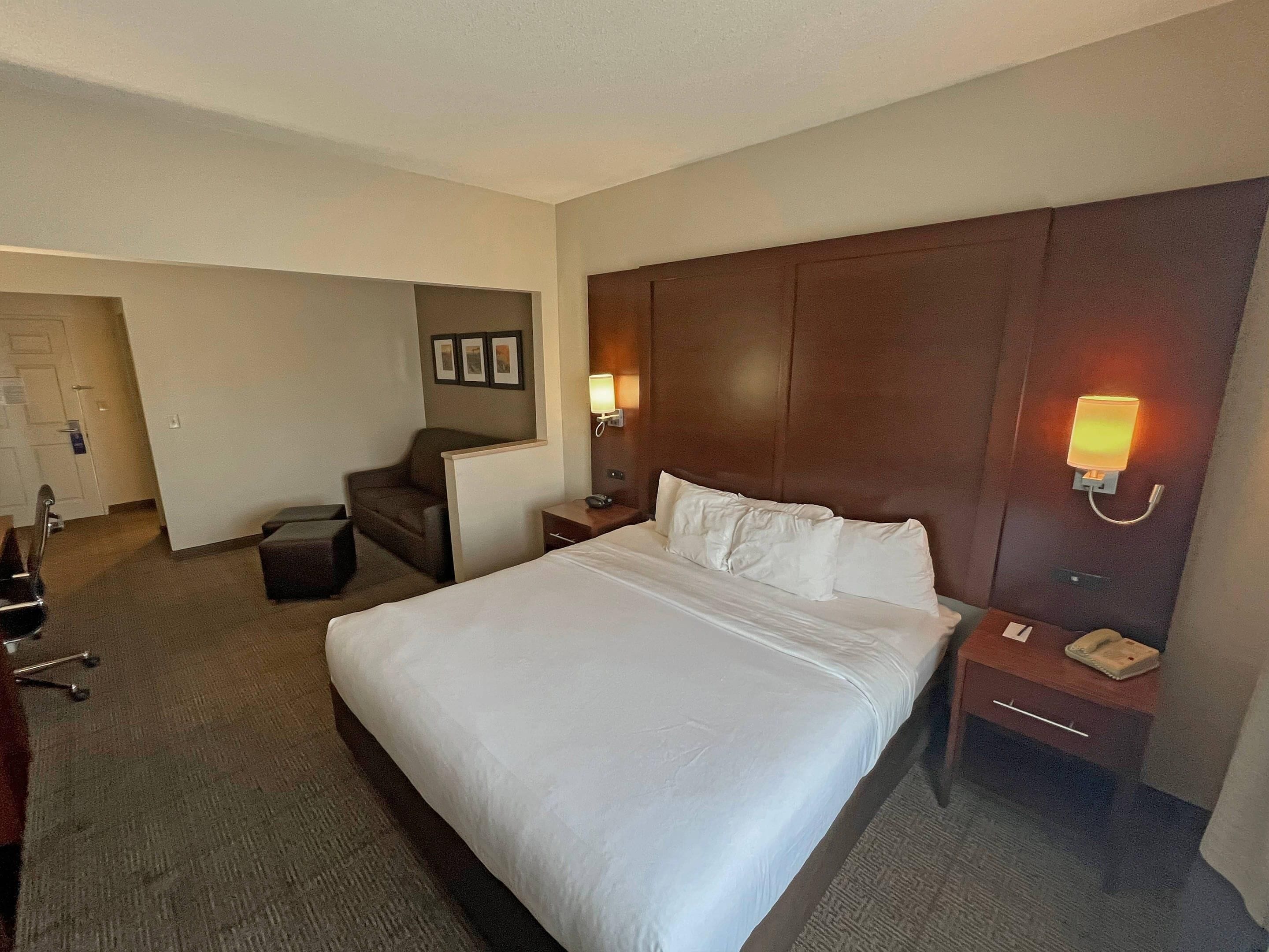 Ein Hotelzimmer mit einem großen Bett, einem Schreibtisch, einem Stuhl und einem Nachttisch mit Lampe.