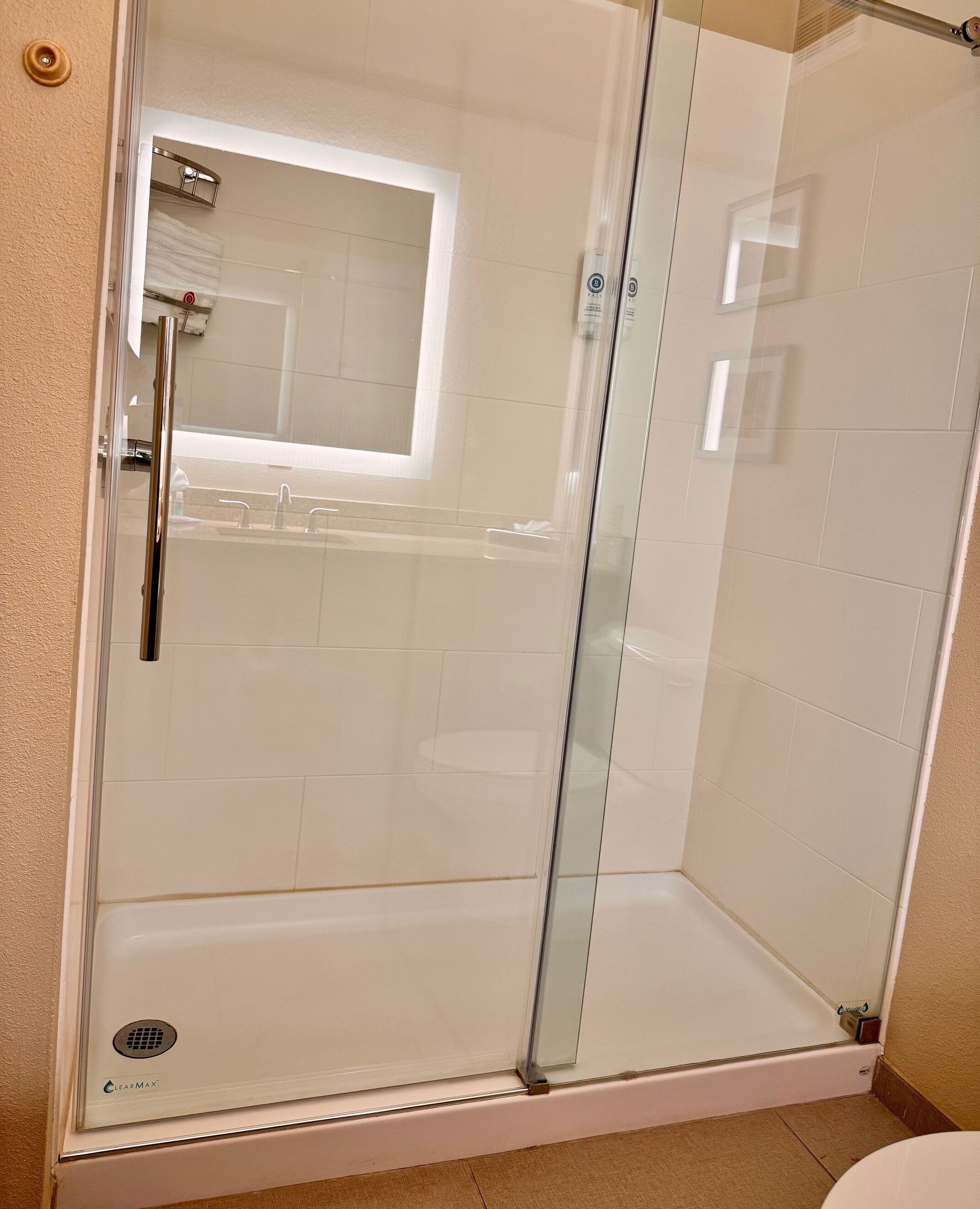 Cabina de ducha con paredes de vidrio que ofrece vista clara del baño, incluyendo un inodoro y un lavamanos.