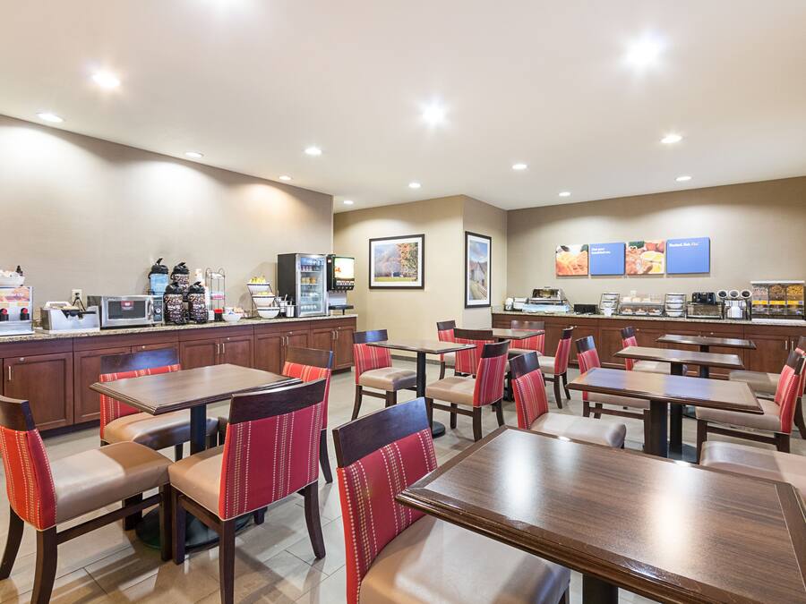 A hotel dining area with multiple tables and chairs, a self-service beverage station, and a buffet counter.