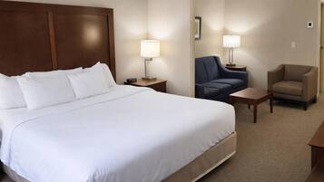 A hotel room with a large bed, two bedside tables with lamps, a blue chair, and a beige armchair.