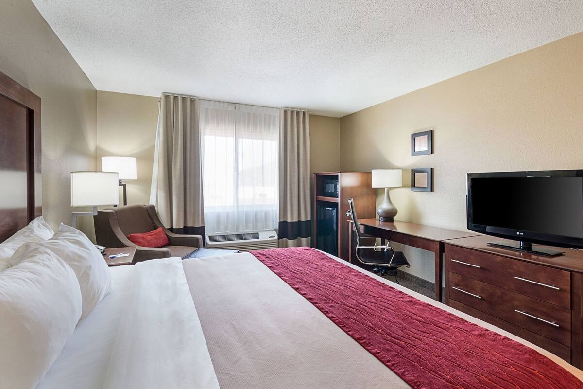 A hotel room with a bed, desk, TV, and a window with curtains.
