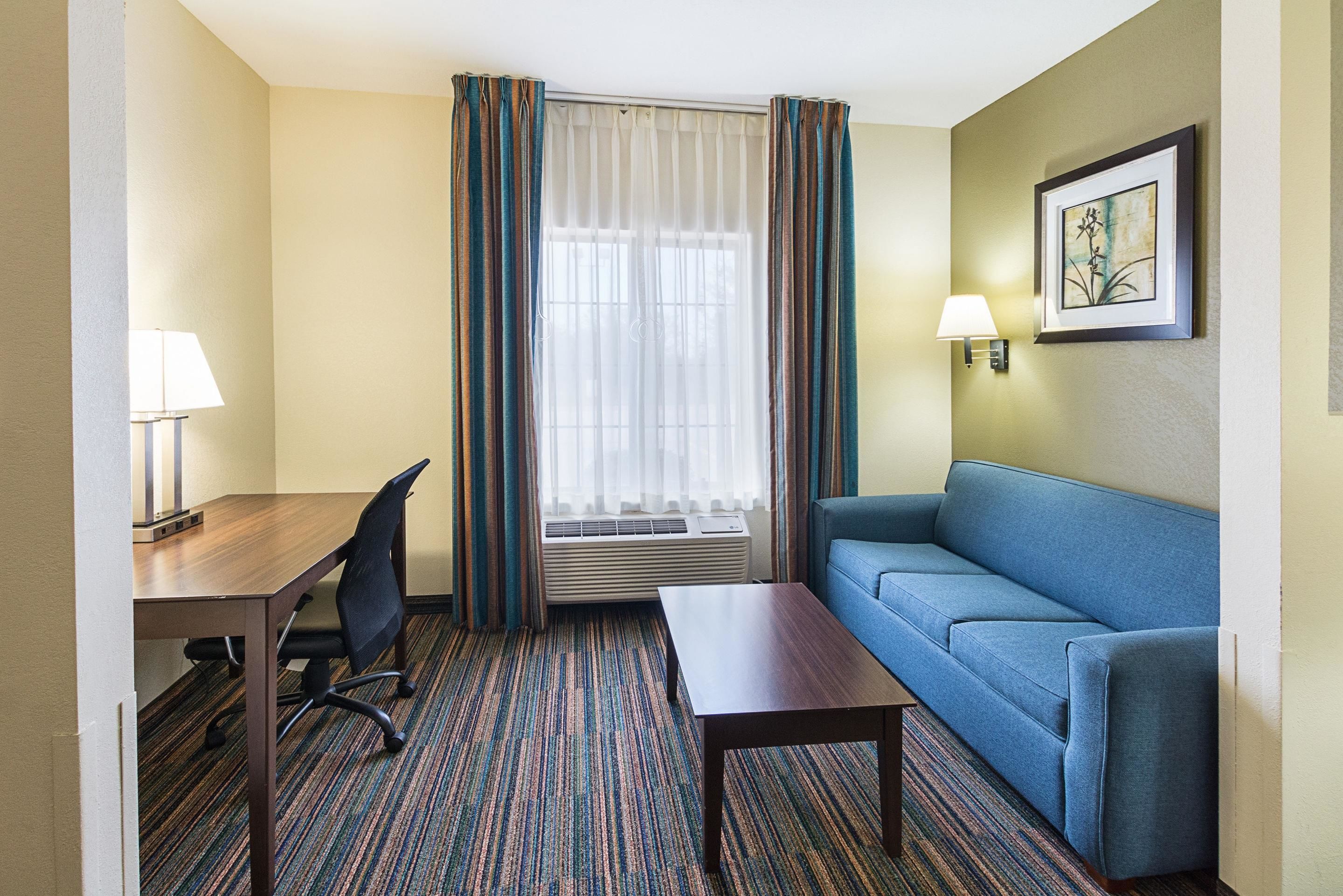 A hotel room with a desk, chair, sofa, and a window with curtains.