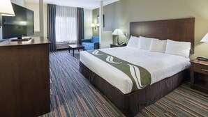 Una habitació d'hotel amb un llit gran, una taula de treball amb televisió, una cadira, una làmpada i una finestra amb cortines.