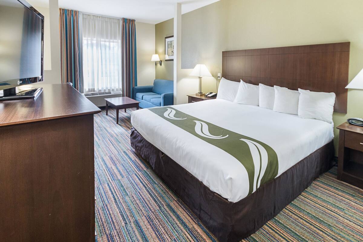 A hotel room with a large bed, a desk, a television, a chair, and a window with curtains.