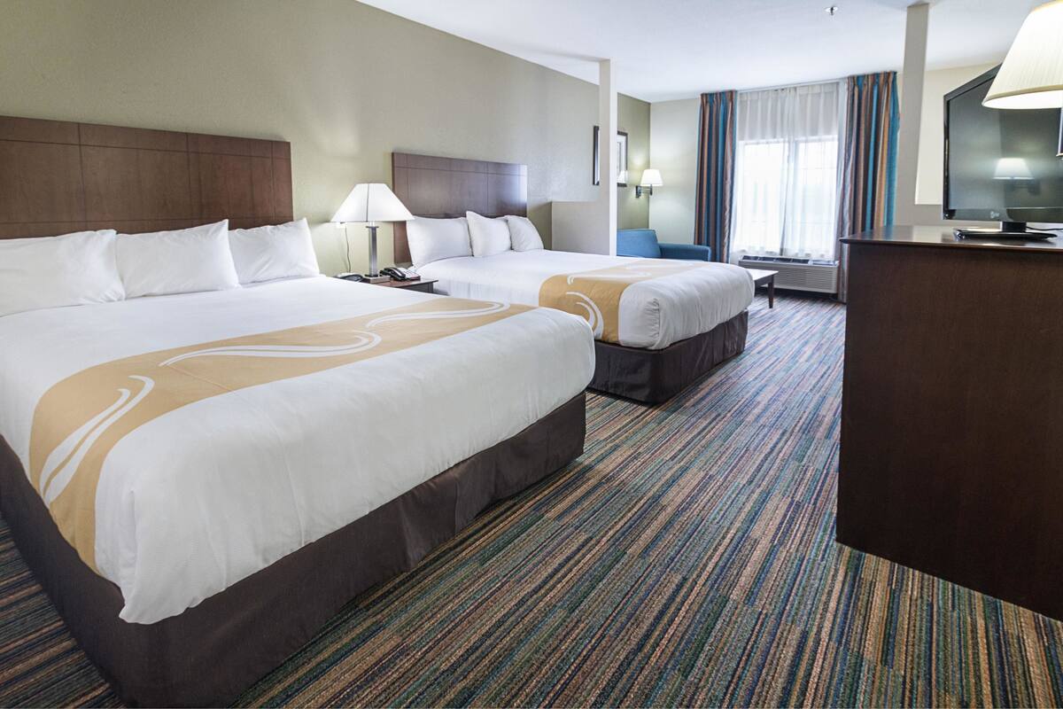 A hotel room with two beds, a desk, a television, and a window with curtains.