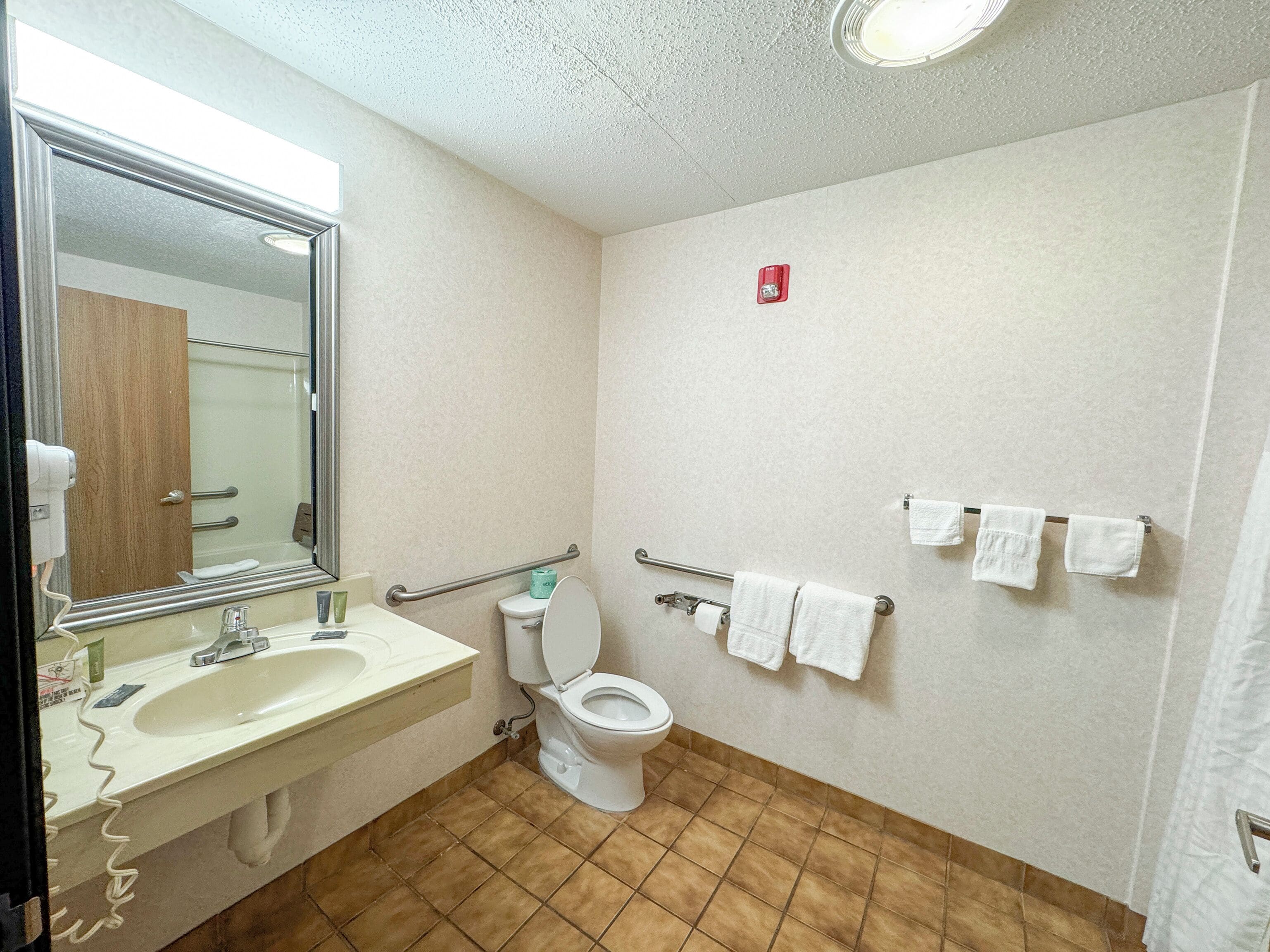 A bathroom with a sink, mirror, toilet, and handrails.