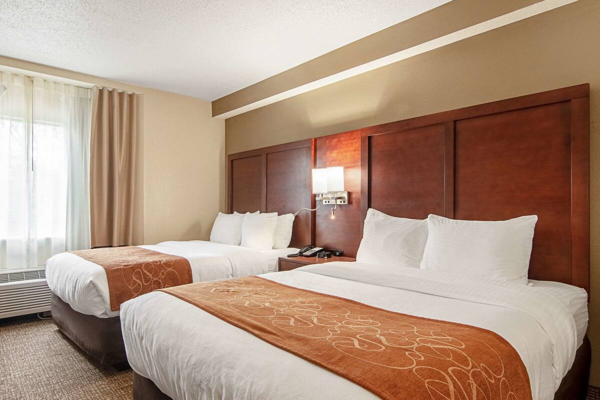 A hotel room with two beds, a nightstand, a lamp, and a phone.