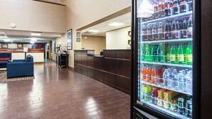 Un hall d  ’hôtel doté d’un réfrigérateur Coca-Cola rempli de diverses boissons, d’un comptoir de réception et d’un espace salon avec des canapés bleus.